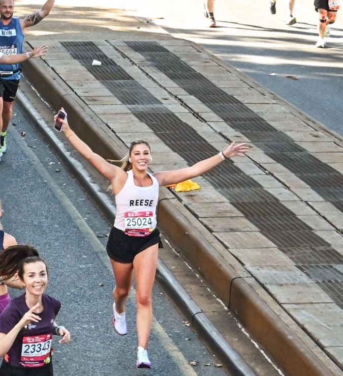 Reese running the NYC Marathon, smiling with arms raised in celebration